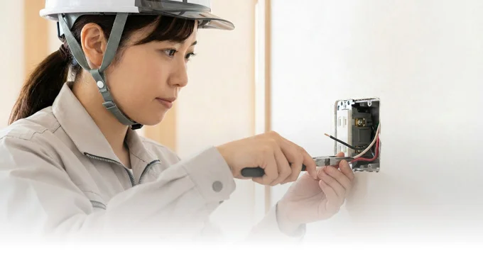 女性電気工事士がコンセントボックスへの結線作業を行っている、手元のクローズアップです。プロの確かな技術と集中力を表現しています。