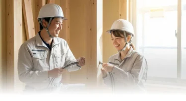 新築住宅の現場で、男女の電気工事士が協力して木材の柱にケーブルを通している様子です。チームワークの良さが伝わる一枚です。